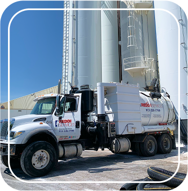Reddi Services vacuum truck parked beside large industrial storage silos